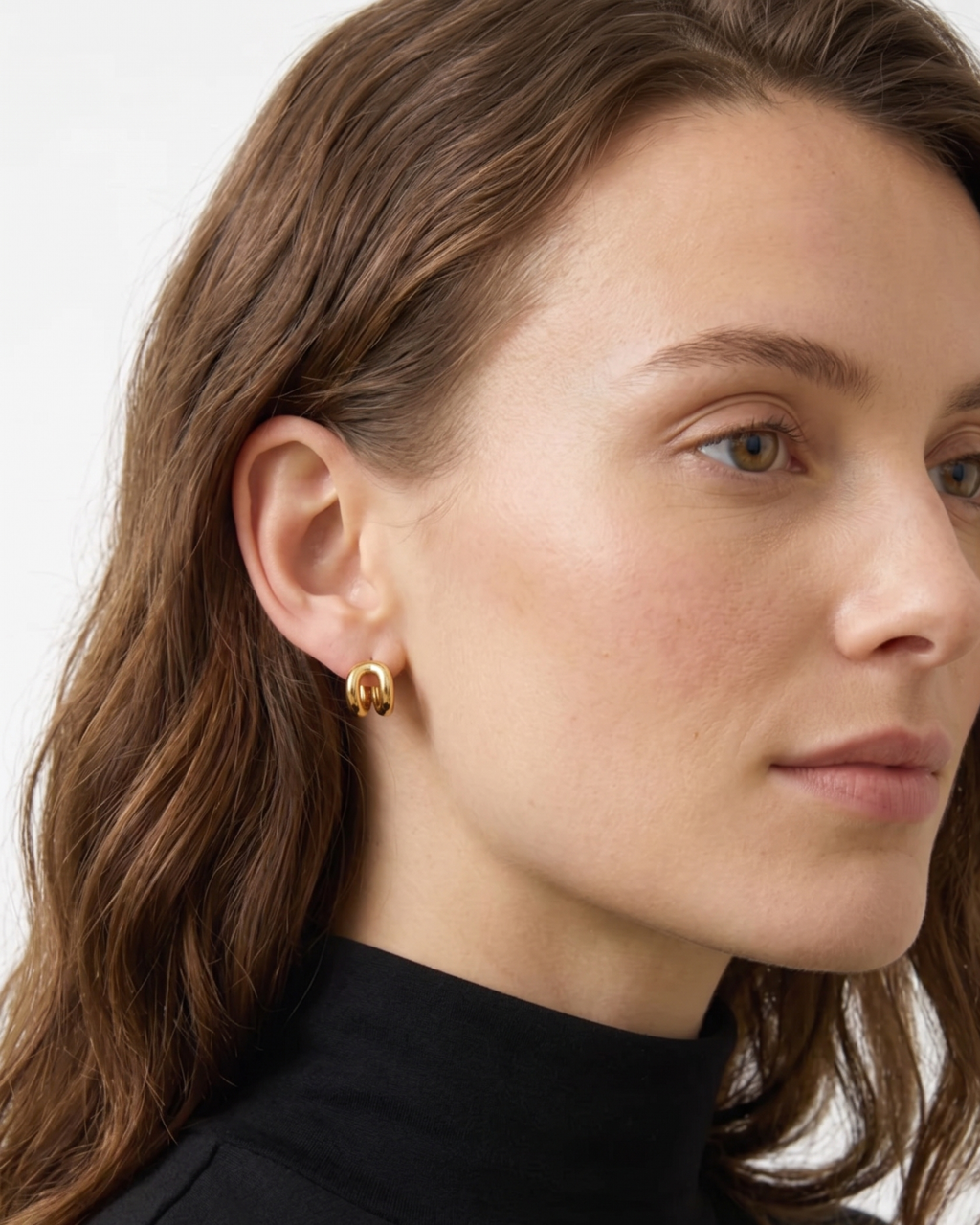 Close-up of a woman wearing gold earrings with a neutral background