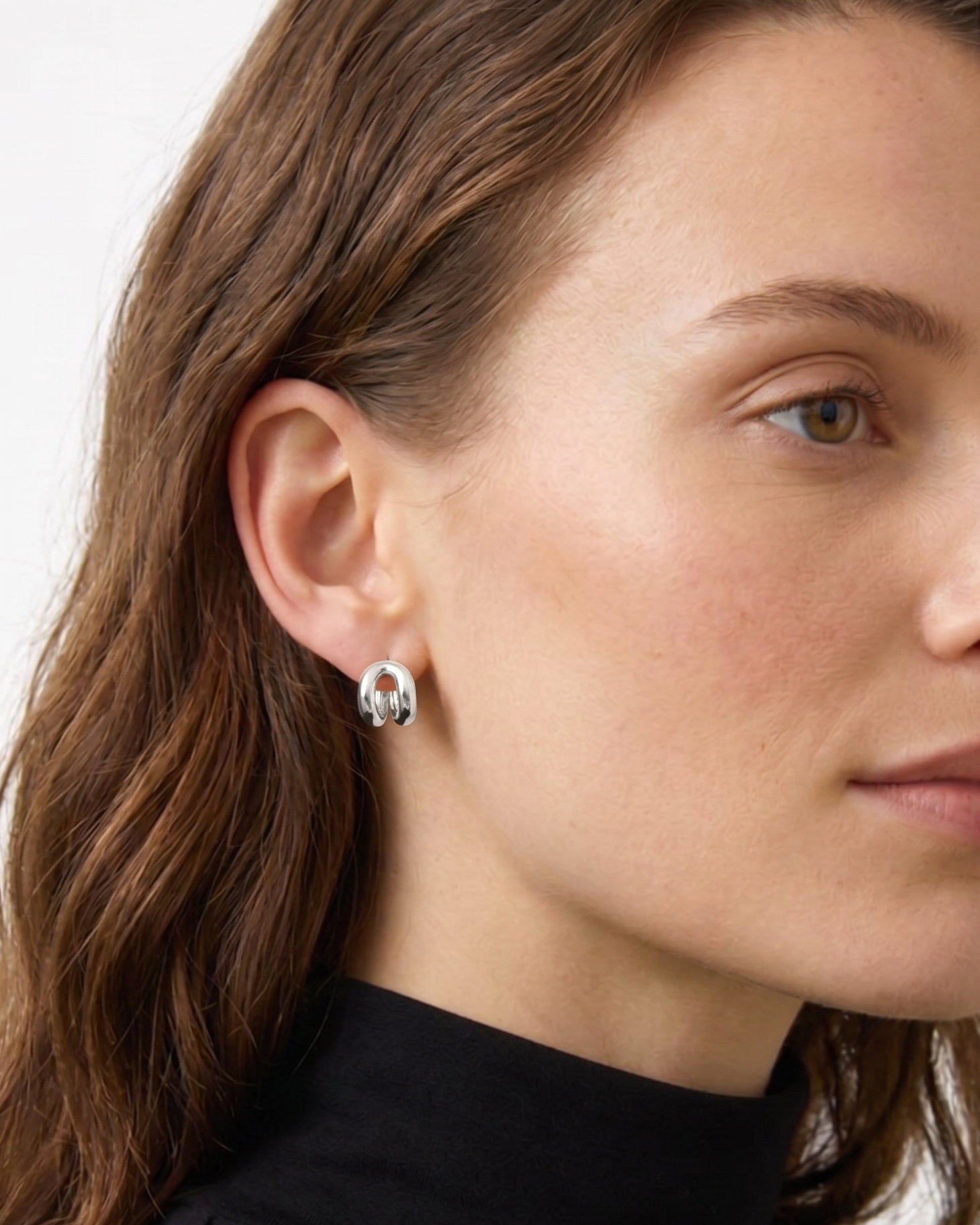 Close-up of a woman wearing silver earrings with a plain background