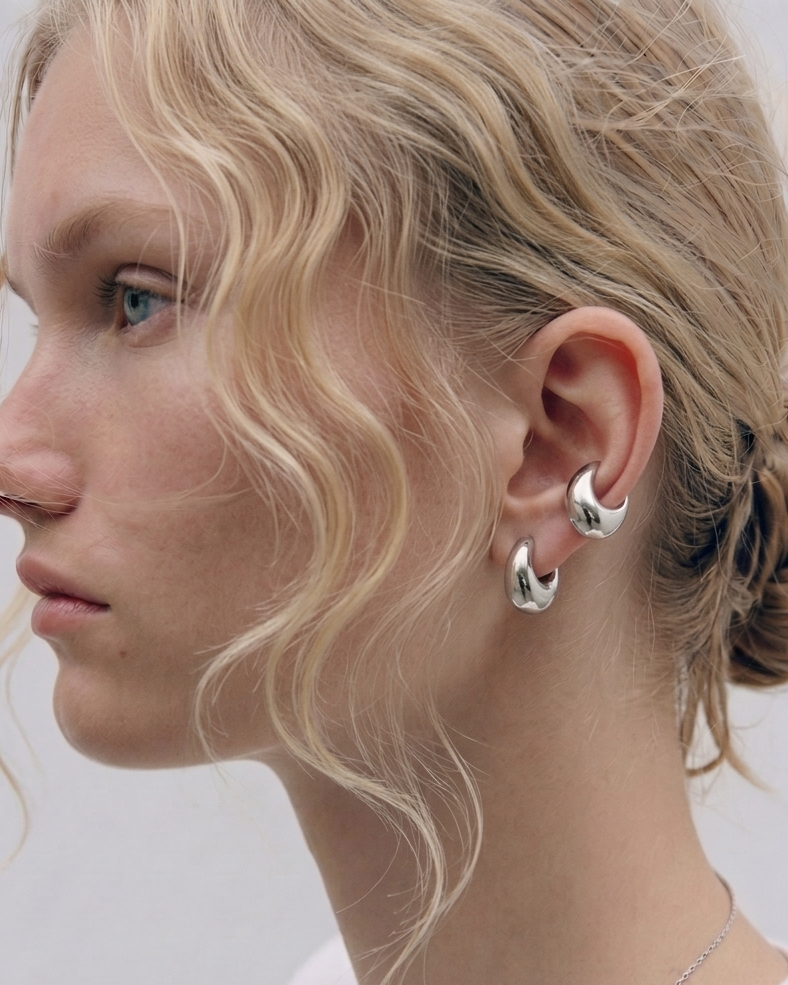 Close-up of a person wearing silver hoop earrings with a plain background