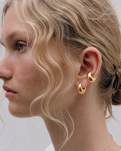 Close-up of a woman wearing gold hoop earrings with a neutral background