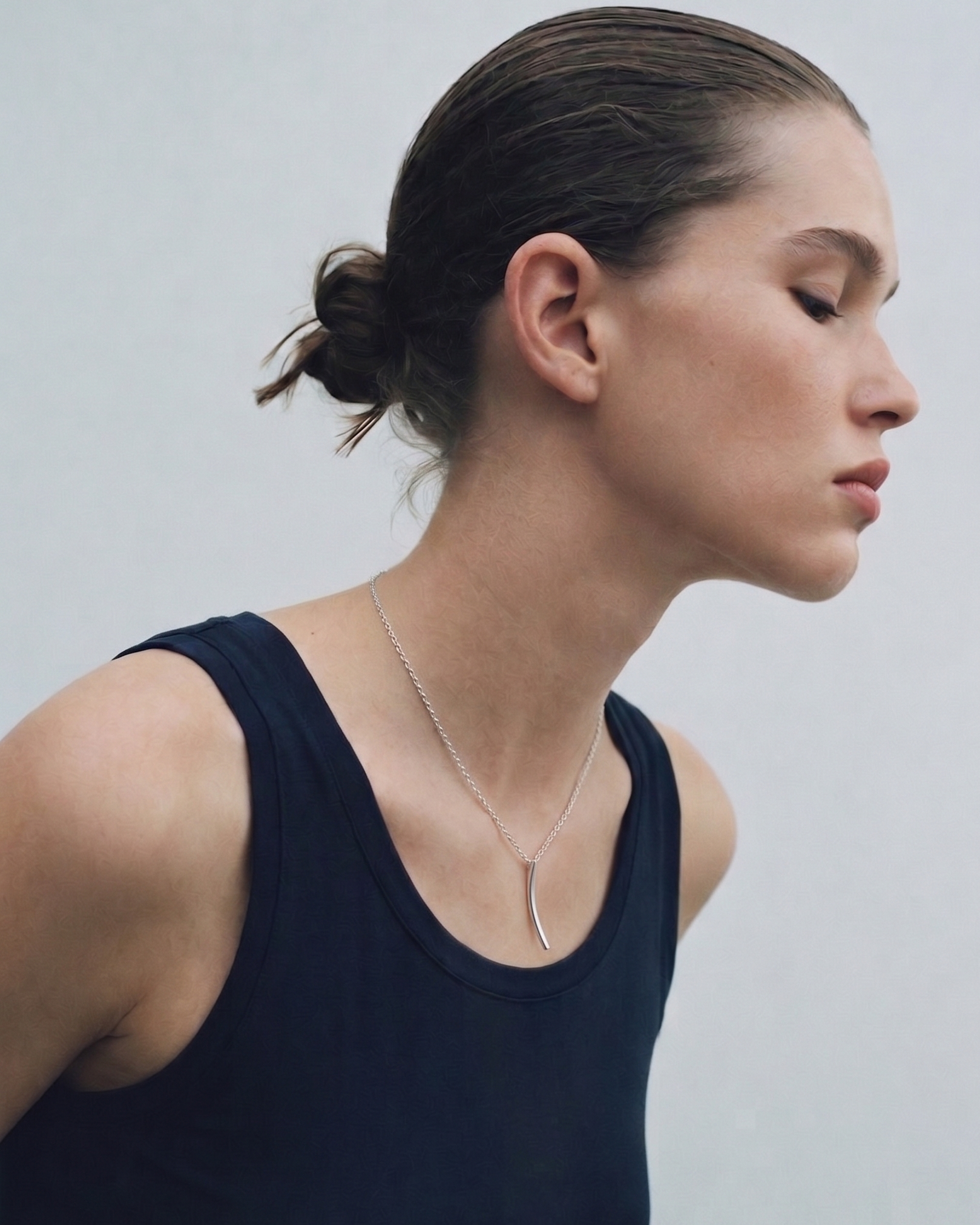 Woman wearing a dark blue tank top and a necklace against a plain background