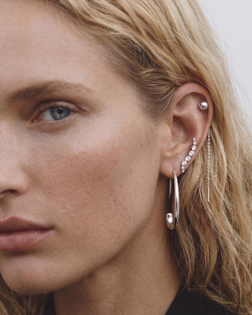 Close-up of a woman wearing multiple earrings with a neutral background