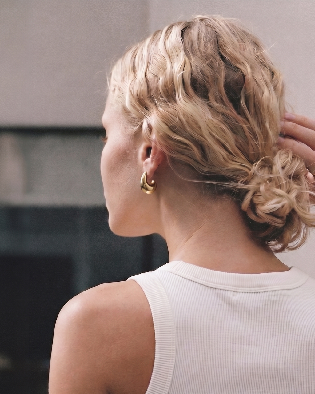 Woman with styled blonde hair in a bun, wearing gold hoop earrings.