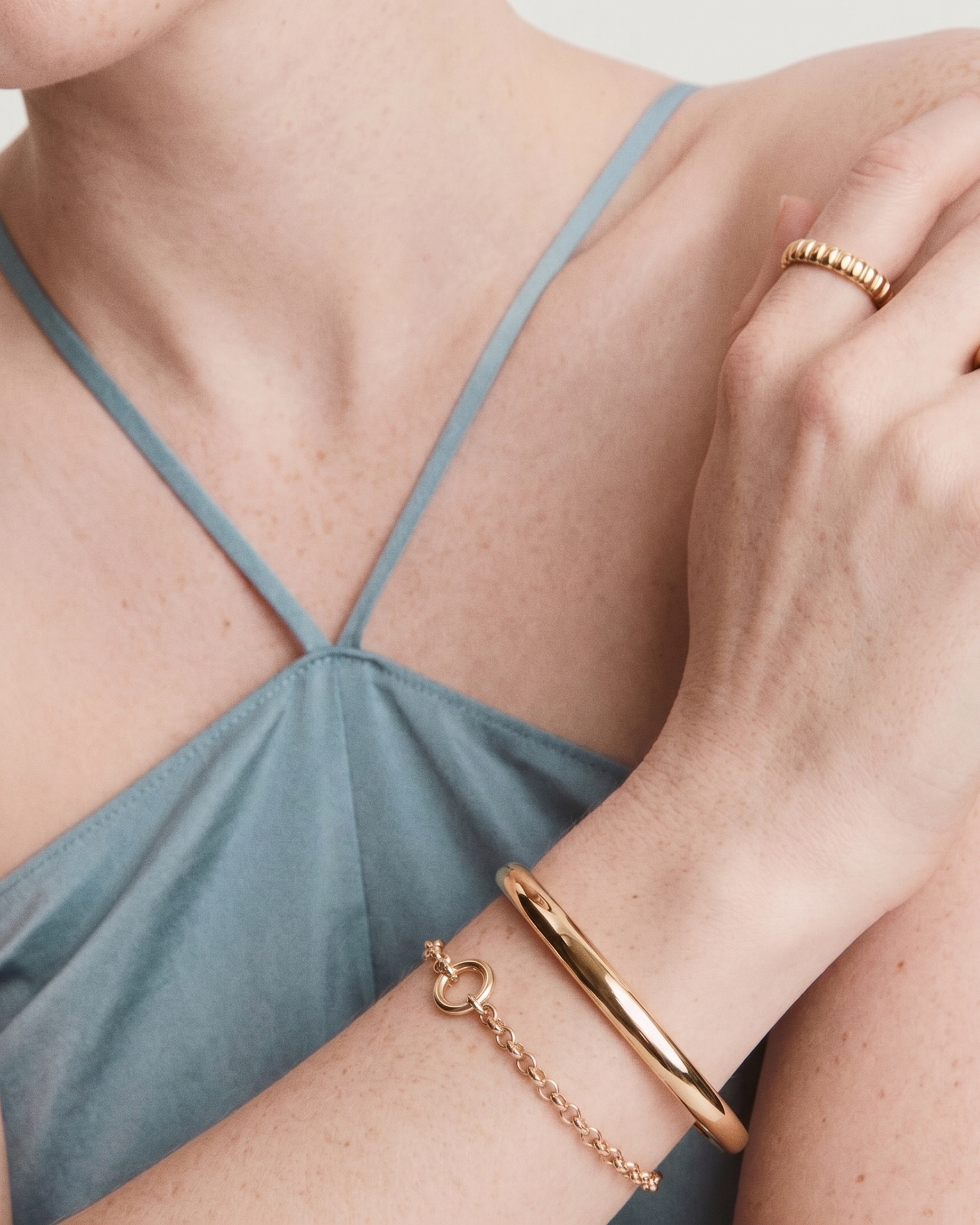 Close-up of a person wearing gold jewelry including rings and a bracelet on a neutral background