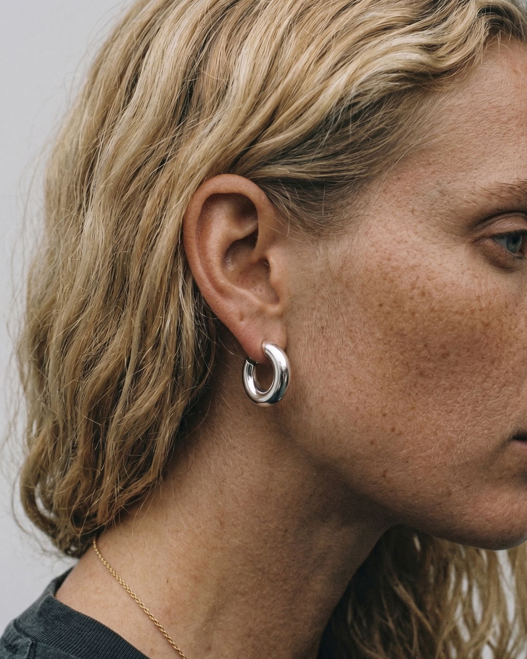 Close-up of a person wearing silver hoop earrings with a neutral background