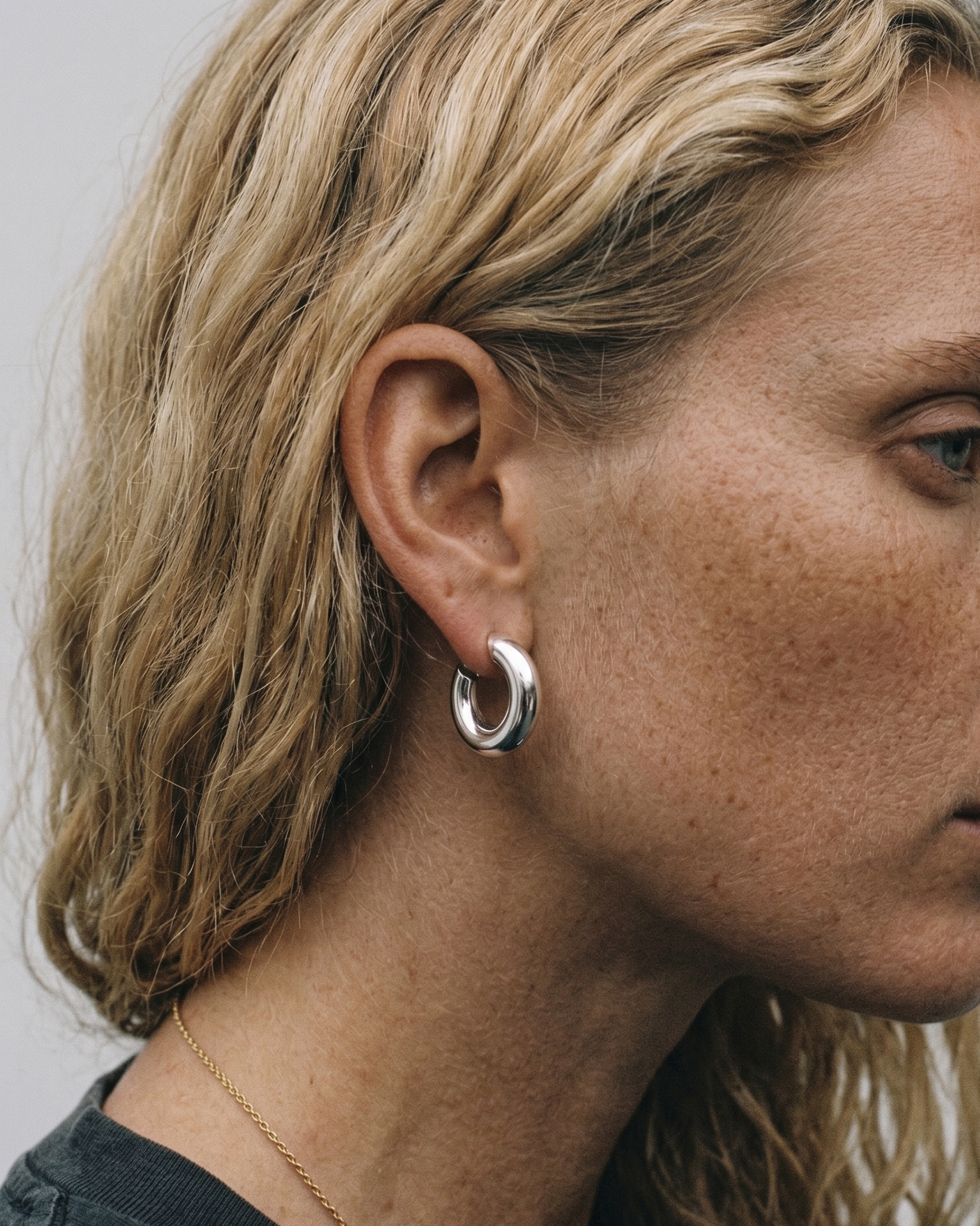 Close-up of a person wearing silver hoop earrings with a neutral background