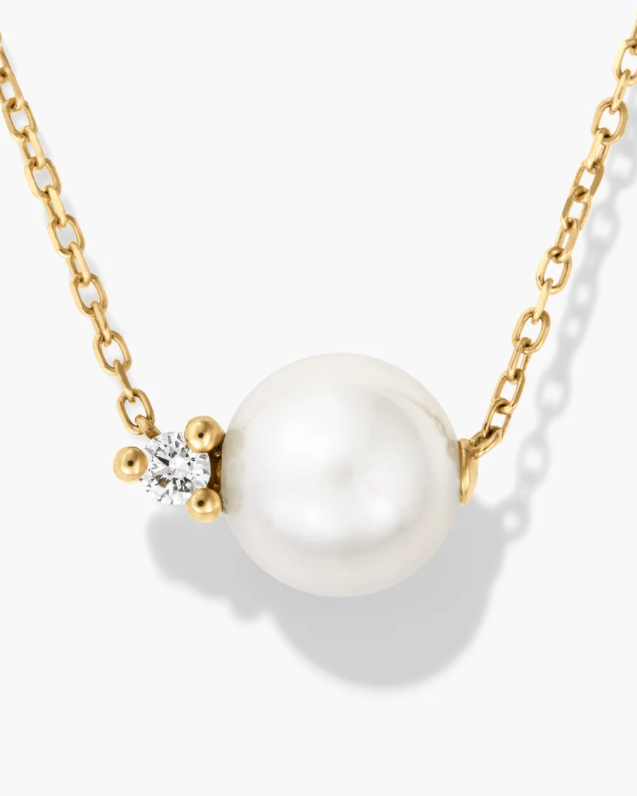 Pearl necklace with gold chain and diamond accent on a white background