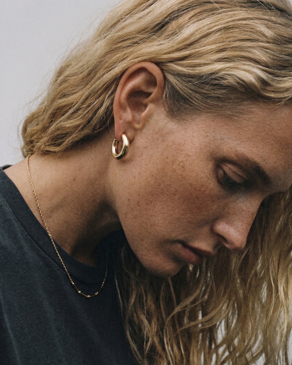 Close-up of a person wearing gold hoop earrings with a neutral background