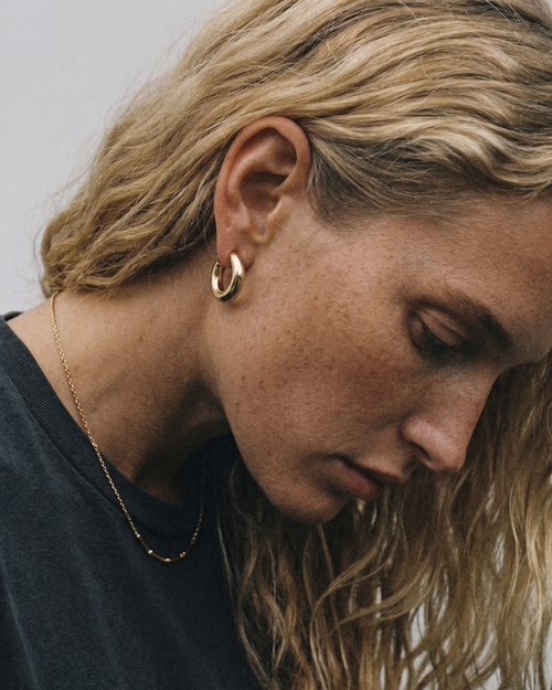 Close-up of a person wearing gold hoop earrings with a neutral background