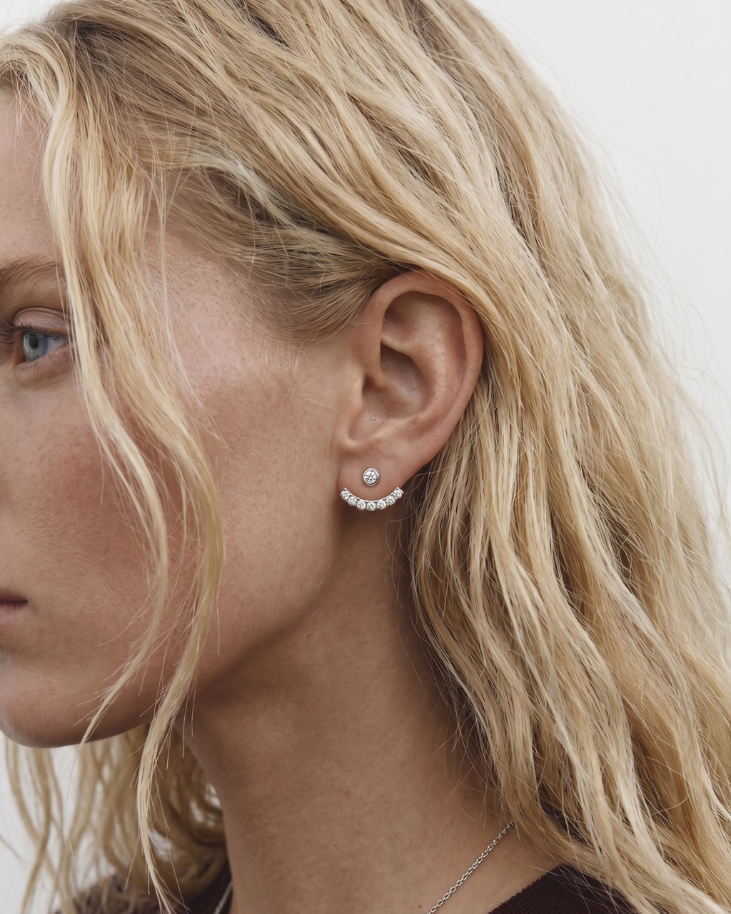 Close-up of a woman wearing pearl stud earrings with a neutral background